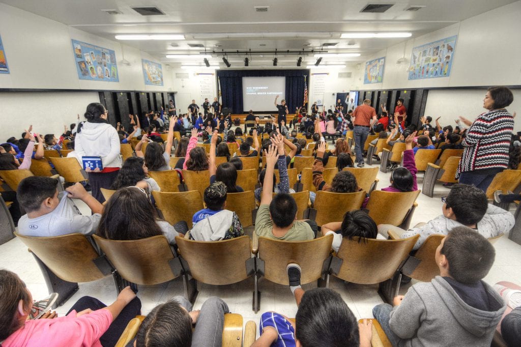 Kids in classroom raise their hands during a FireSmart:LA lecture from MySafe:LA public safety officers.